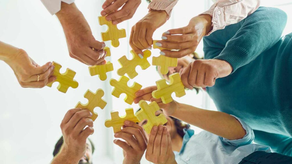 Wiele rąk trzymających drewniane puzzle, które tworzą wspólną całość – metafora współpracy i budowania sieci kontaktów przez ZZP w Holandii.